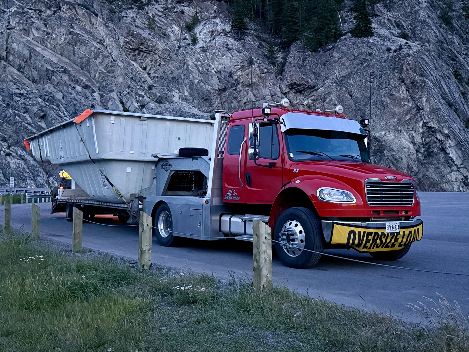 Red truck hauling oversized load near rock face